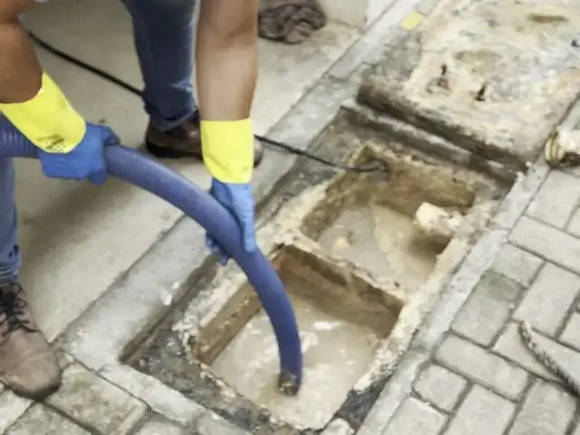 Técnico aspirando caixa de esgoto com mangote do caminhão limpa fossa